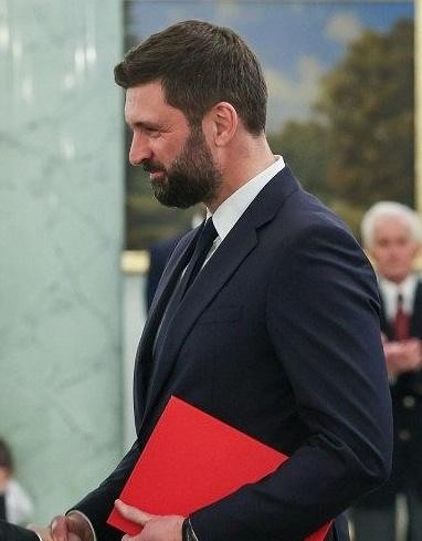 Nikodem Rachoń podczas spotkania dotyczącego polityki międzynarodowej, w tle elementy biura lub sali konferencyjnej.