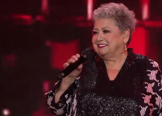Ewa Bem śpiewająca z pasją na scenie podczas koncertu jazzowego, z mikrofonem w dłoni i oświetleniem scenicznym.