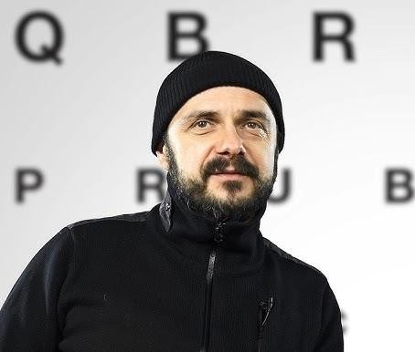Arkadiusz Jakubik jako wokalista zespołu Dr Misio podczas energetycznego koncertu na żywo, otoczony dynamicznym oświetleniem sceny.