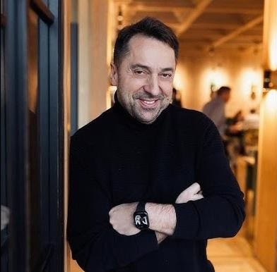 Marcin Miller uśmiechający się ciepło w naturalnym otoczeniu, oddający jego optymizm.