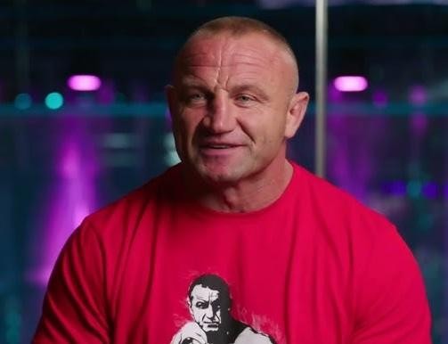 Alt: Mariusz Pudzianowski w klatce MMA, prezentujący swoją siłę i determinację podczas walki.