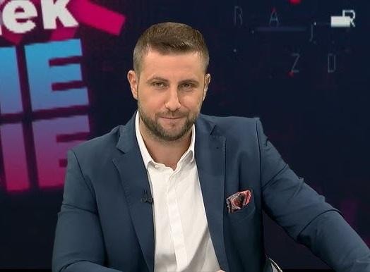 Miłosz Kłeczek w studiu telewizyjnym, gestykulujący podczas dynamicznej debaty, oddający jego intensywny styl dziennikarski.