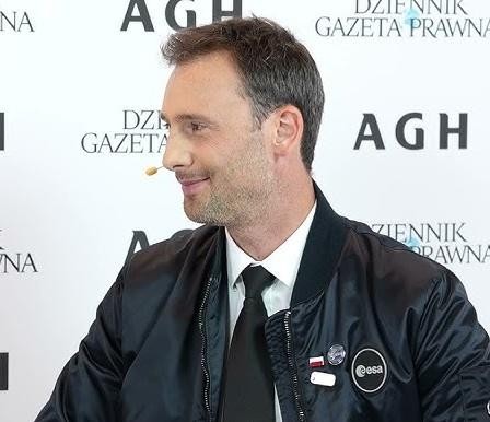 Sławosz Uznański uśmiechnięty, przeglądający swój profil na Instagramie @astro_slawosz na tablecie, z widoczną liczbą obserwujących, w tle subtelne nawiązanie do kosmosu.