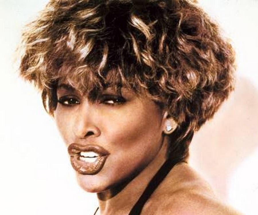 Tina Turner w czerwonej, falbaniastej sukni podczas energetycznego występu na scenie w latach 80., z charakterystyczną fryzurą i intensywnym wyrazem twarzy.